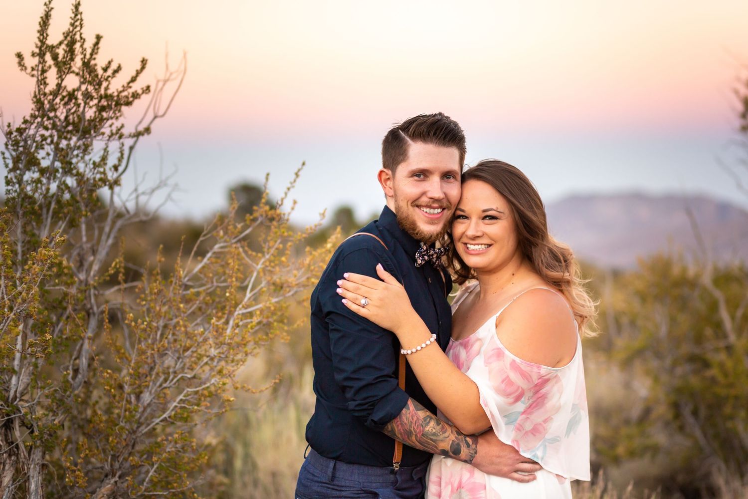 Romantic couple embracing at sunset in a desert landscape with mountains in the background.