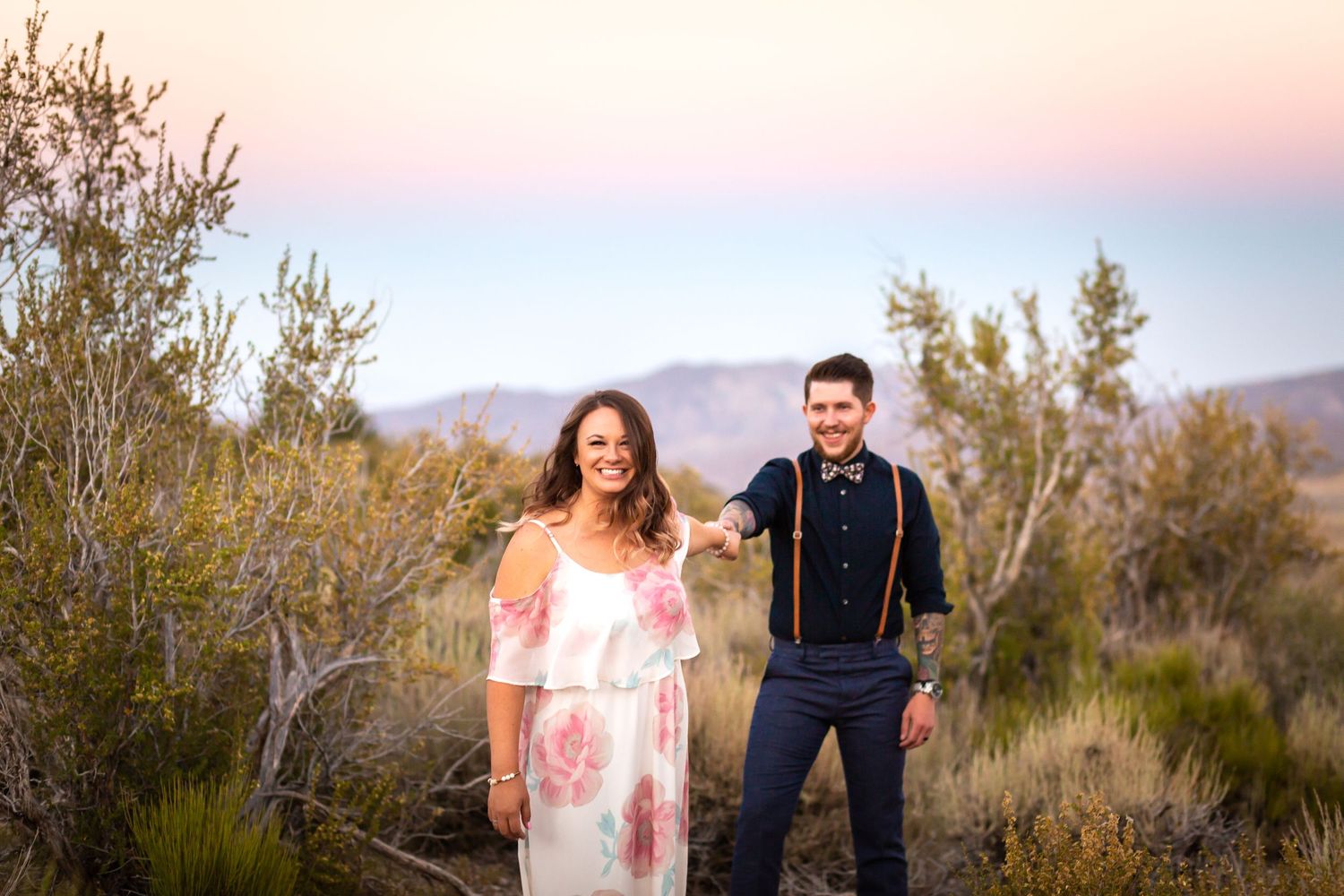 Playful engagement photo in desert with mountains and pink sky.