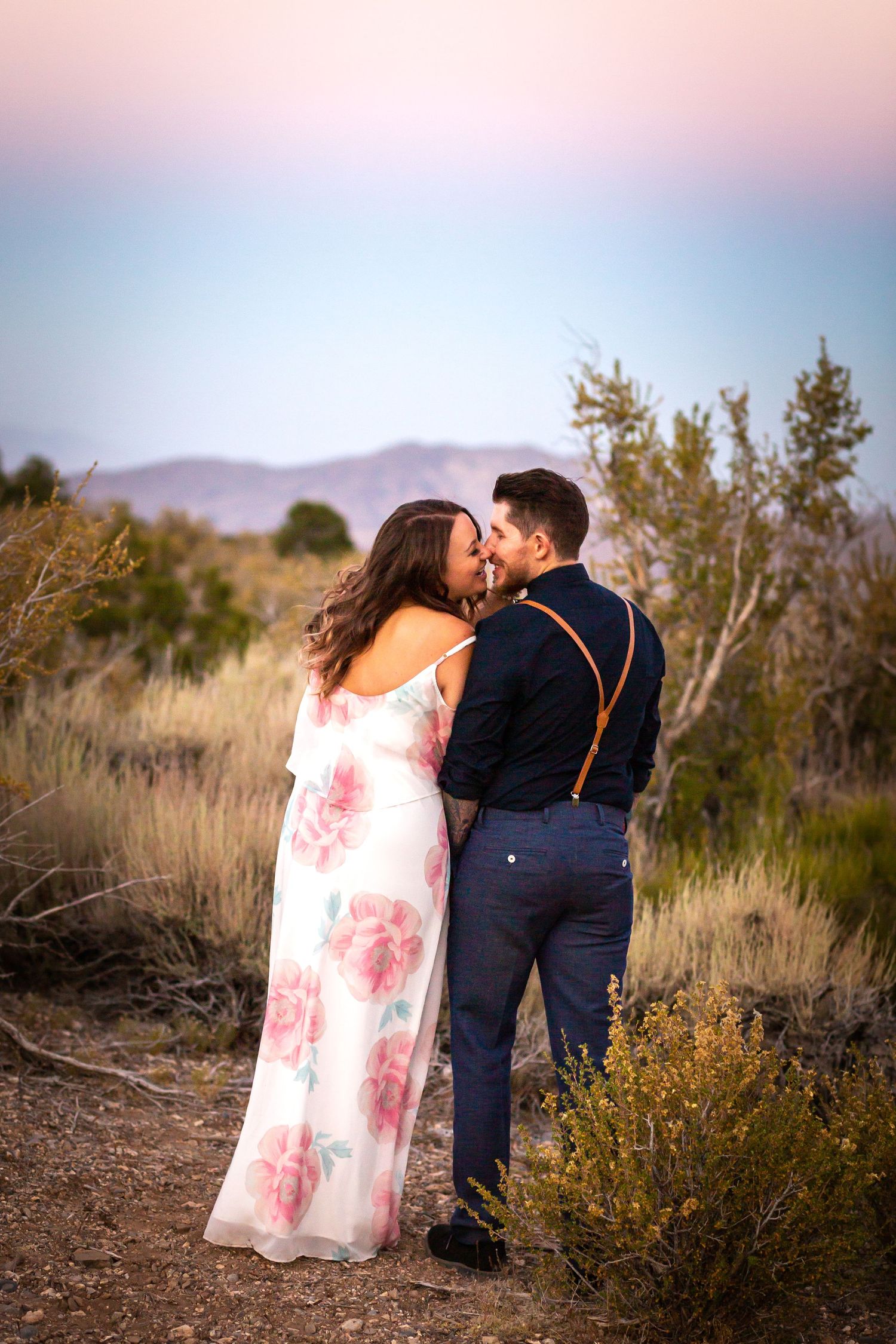 Romantic desert portrait with couple in formal wear against pink sky.