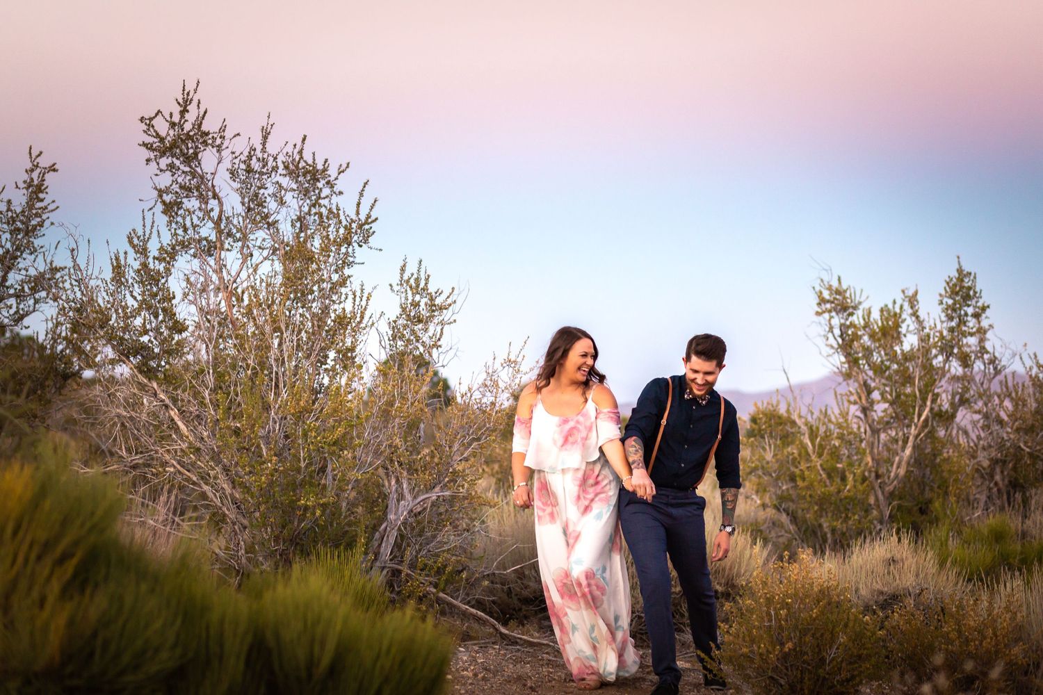 Couple walking hand in hand through desert brush at sunset.