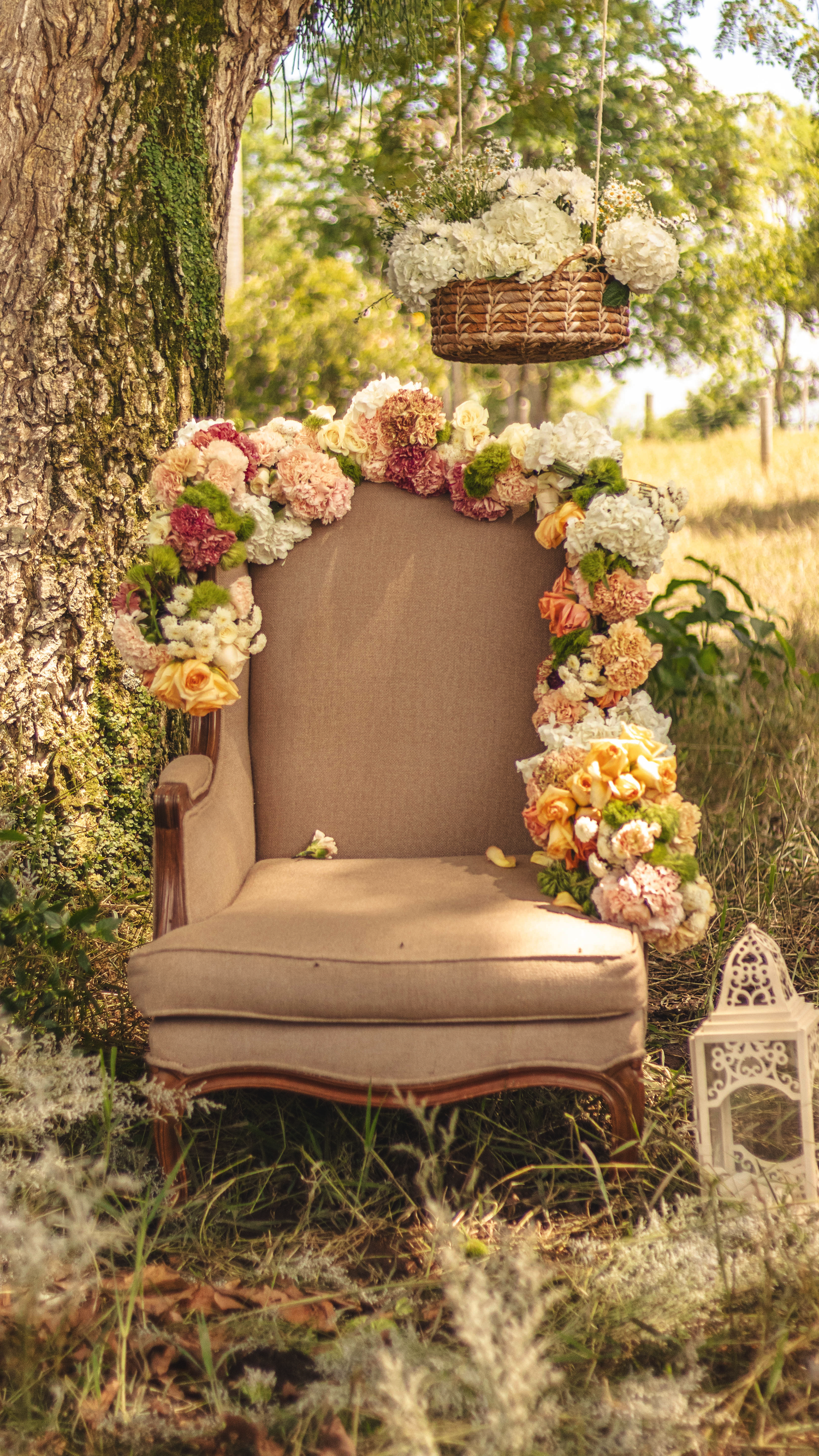 Vintage armchair decorated with pastel floral garland and lantern in dreamy outdoor setting.