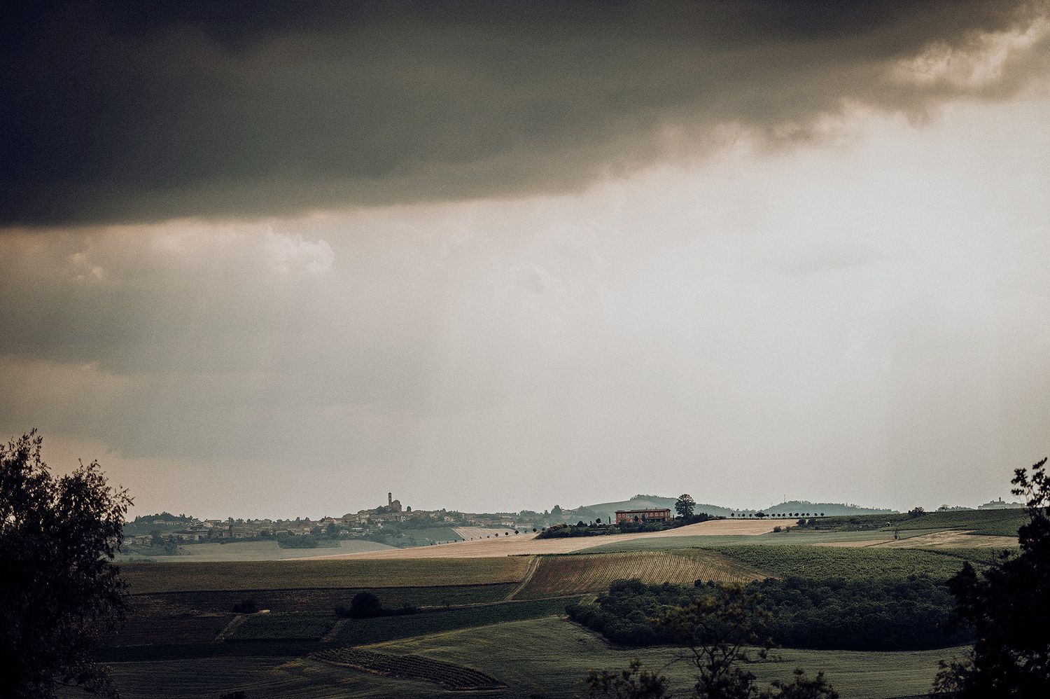 Dramatic stormy sky over vast open farmland with a distant village silhouette on the horizon.