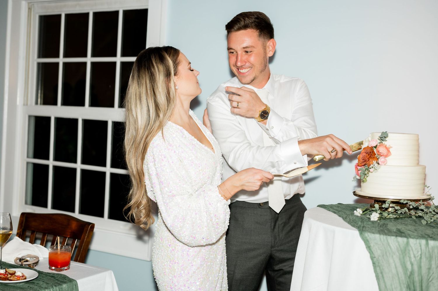 Joyful wedding cake cutting moment captured in a bright indoor setting.