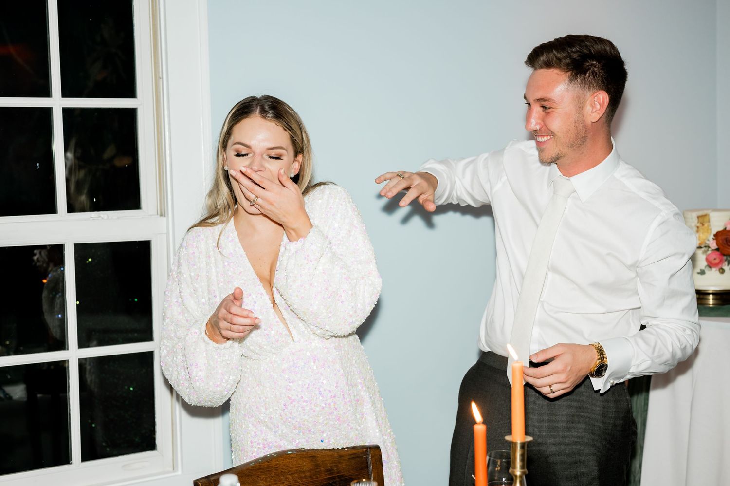 Couple sharing laughs during traditional wedding cake cutting ritual.