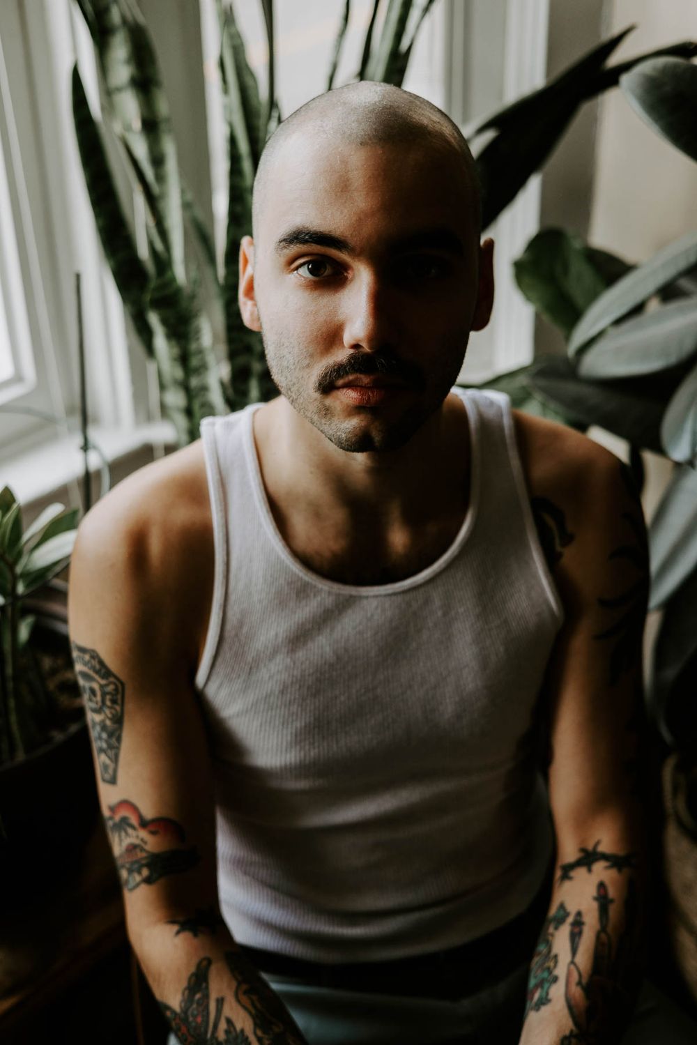 Close-up portrait with natural lighting showing person in gray tank top near window with plants.