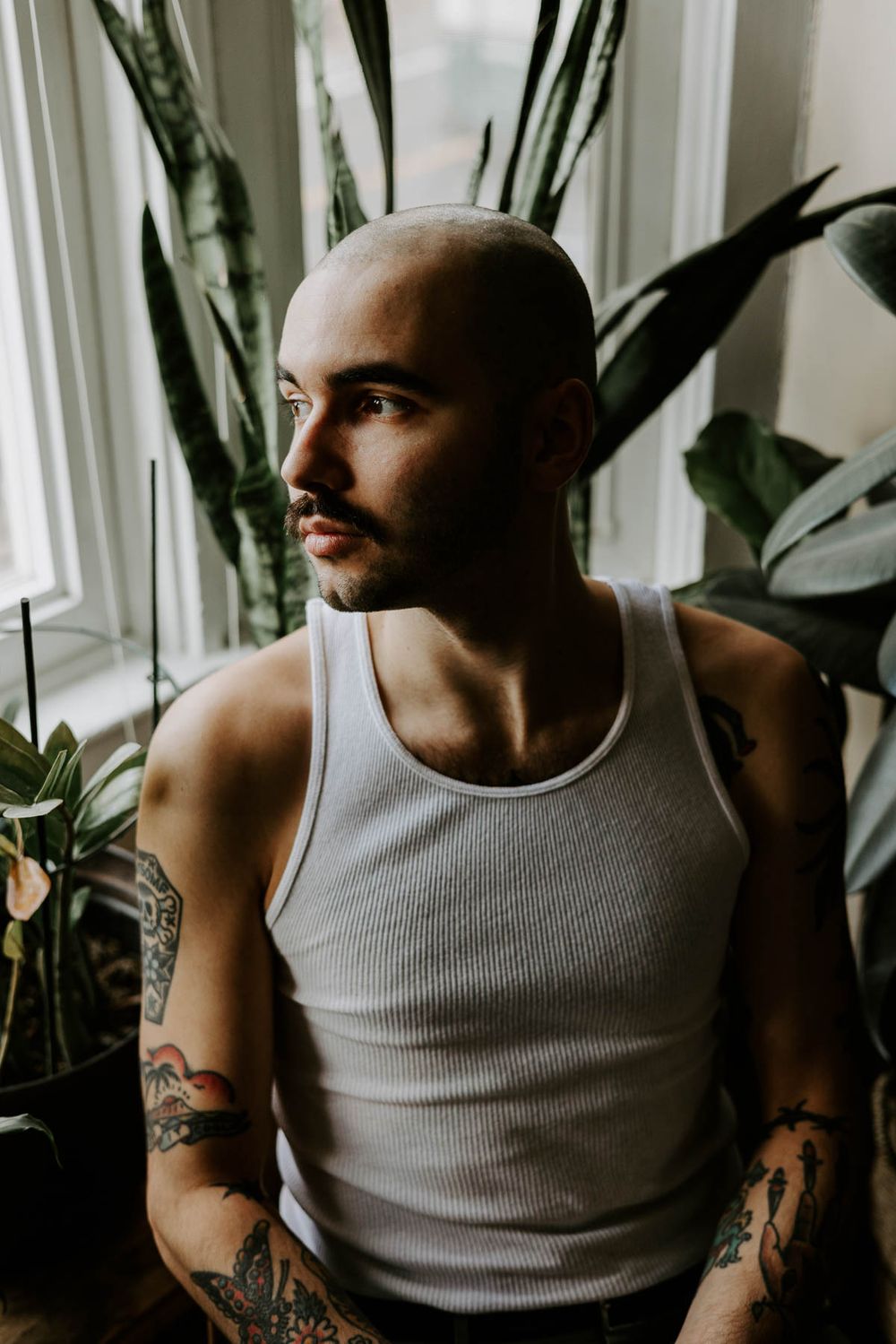 Artistic portrait showing person with mustache in tank top against window light.