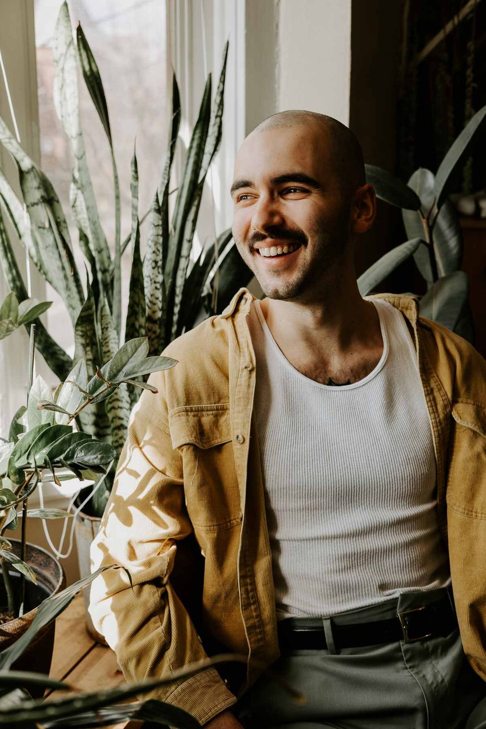 Casual portrait against window with indoor plants showing genuine smile.