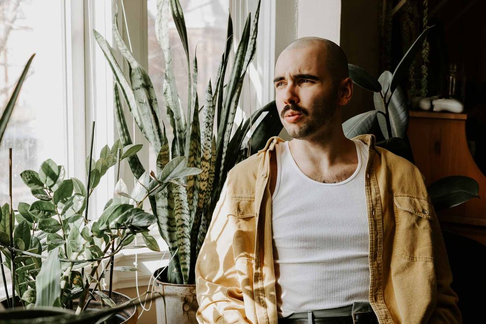 Moody portrait by window featuring houseplants and natural lighting.