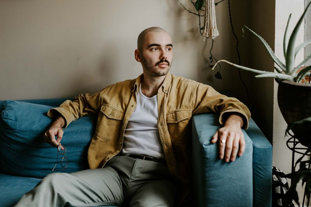 Atmospheric portrait on blue couch with gallery wall in background.