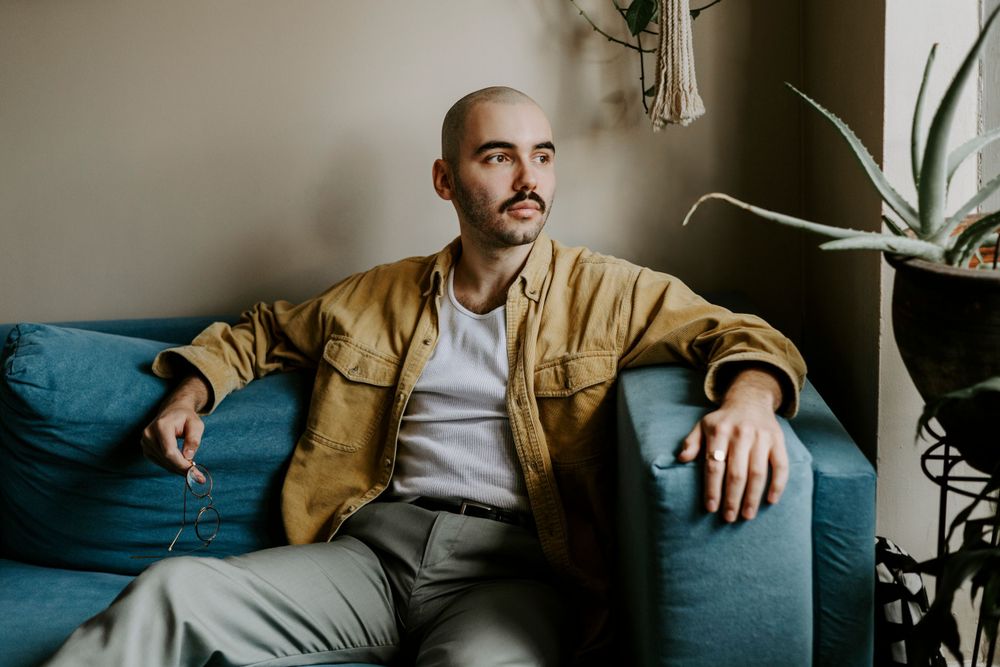 Relaxed indoor portrait showing tan jacket and white sweater against blue couch.