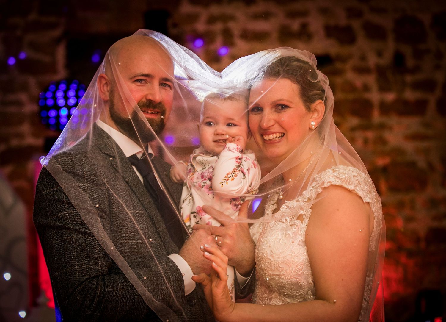 Wedding celebration with colorful lighting and stone wall backdrop during evening reception.