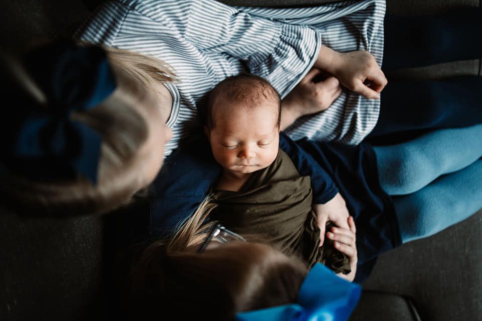 Newborn baby boy surrounded by siblings at a calm, cozy lifestyle newborn session in Knoxville, TN.