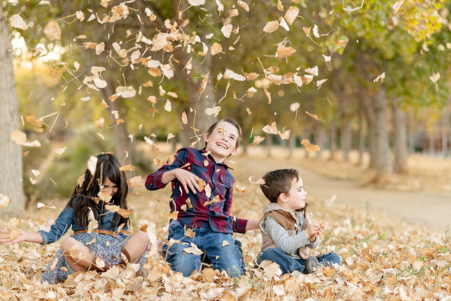 Playful autumn photo session with people tossing leaves in golden sunlight.