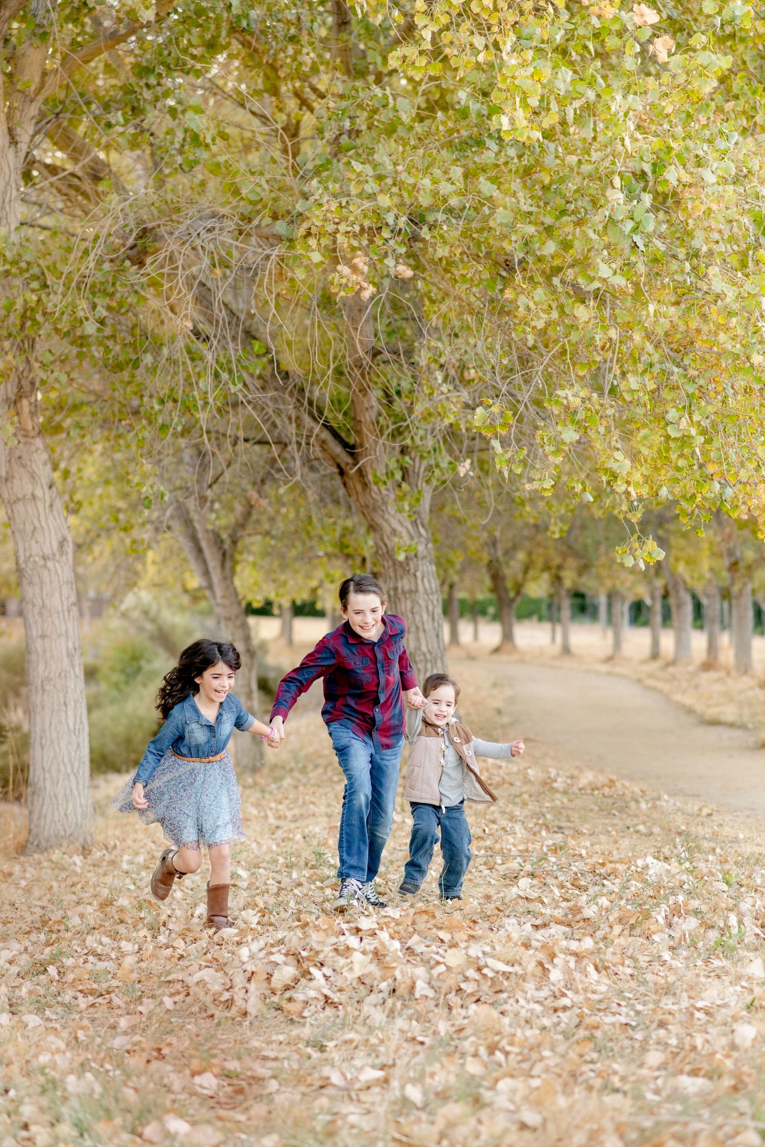 Children run and play together on leaf-covered path under autumn trees.