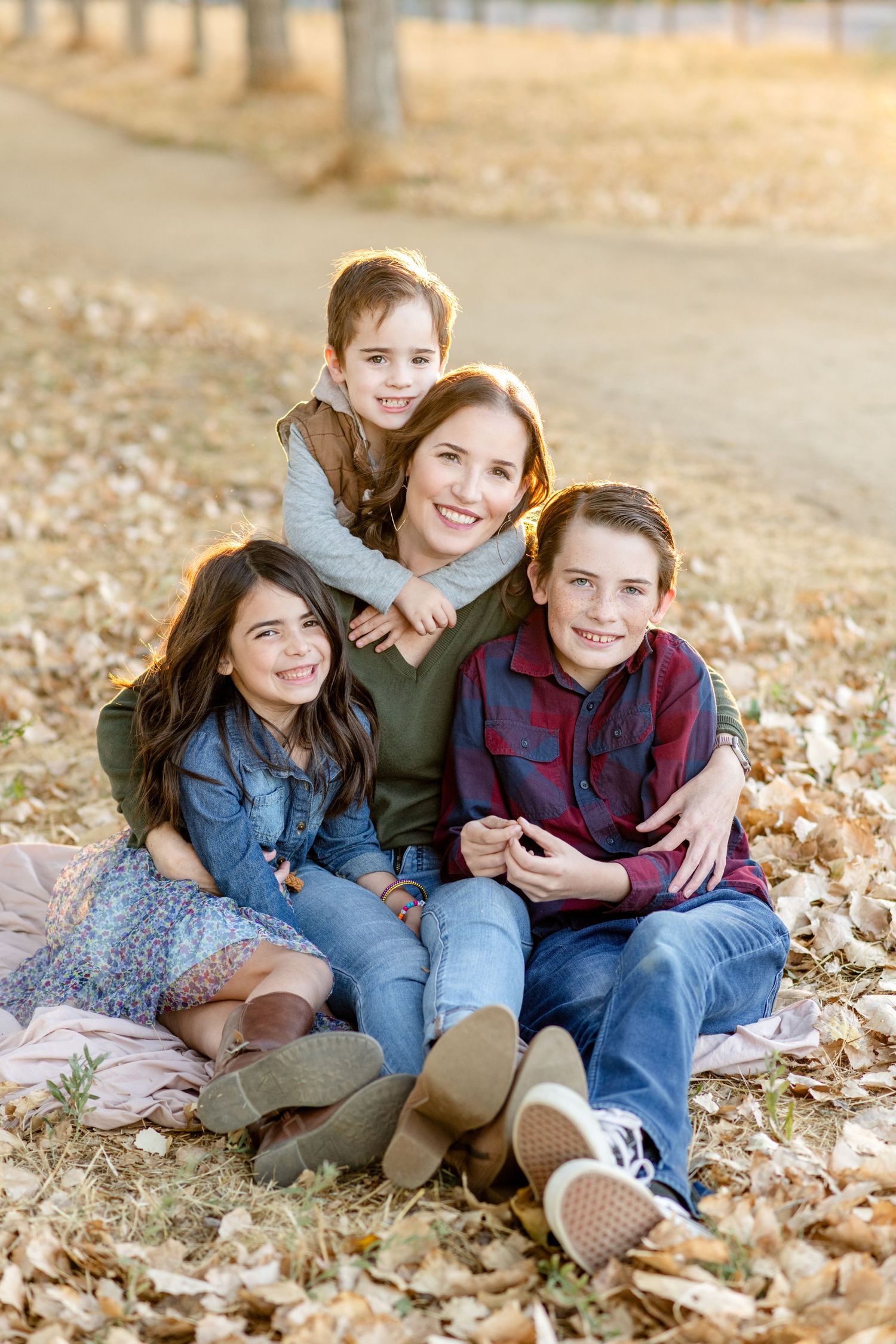 Family group sitting together on fallen autumn leaves during outdoor photo session.
