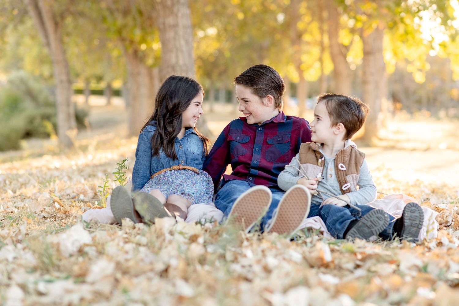 Three children share joyful moment while sitting in fallen autumn leaves.