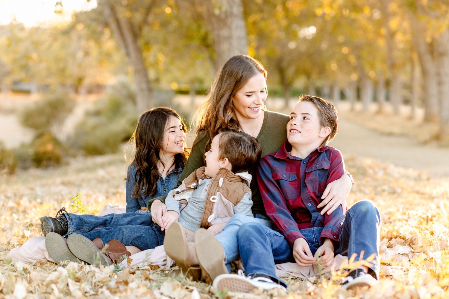 Family laughs together while sitting in fallen autumn leaves.