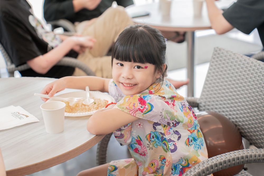 Child in colorful butterfly print dress enjoys meal at restaurant table.