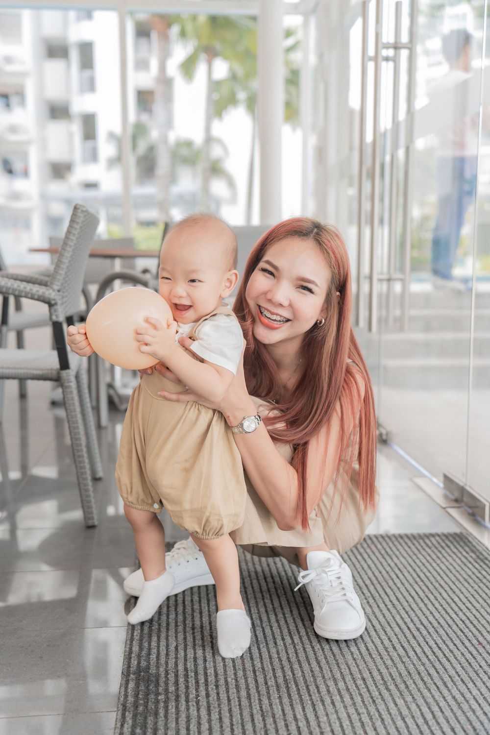 Mother and baby in casual attire pose together in bright indoor setting.