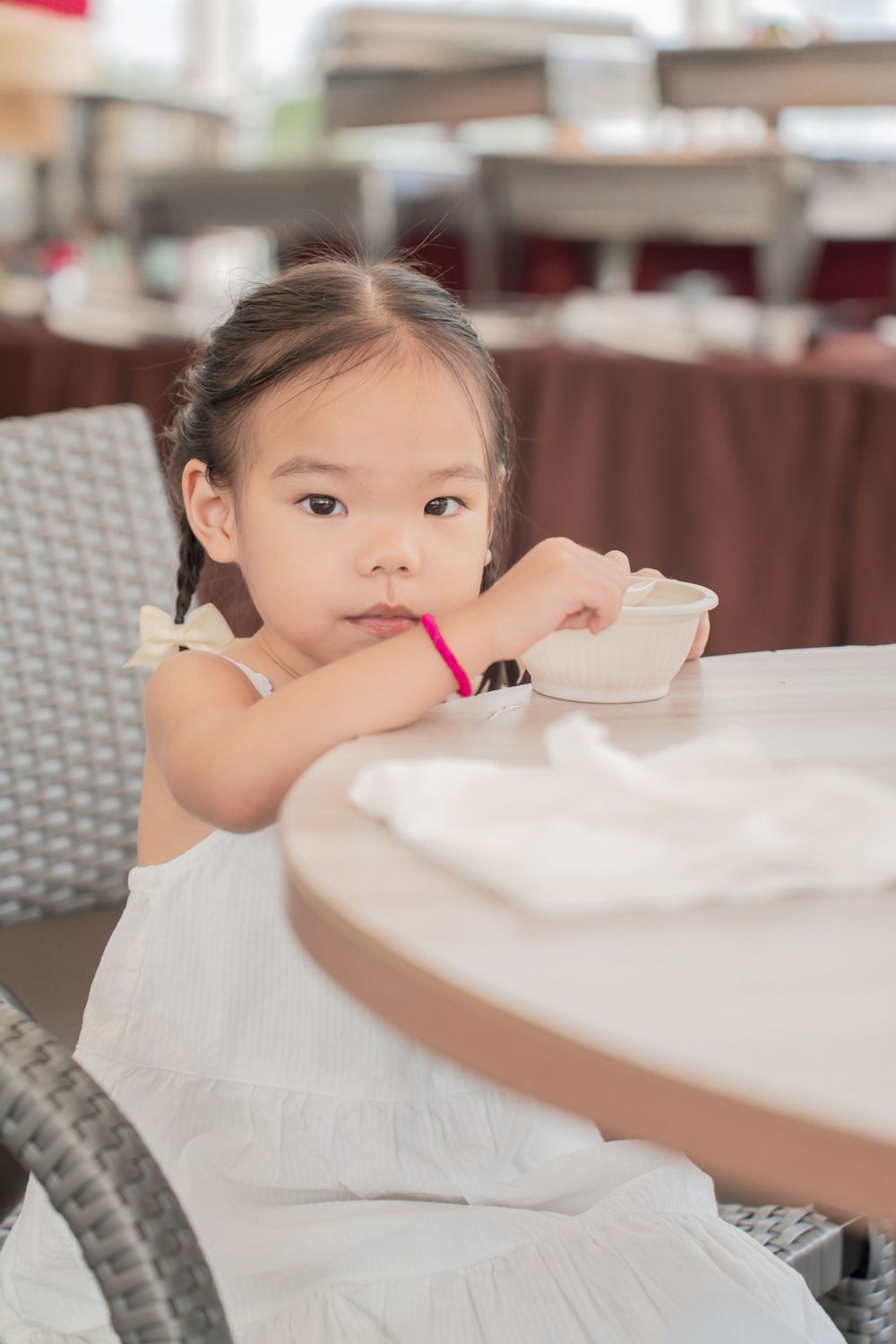 Young child in white dress reaches across restaurant table.