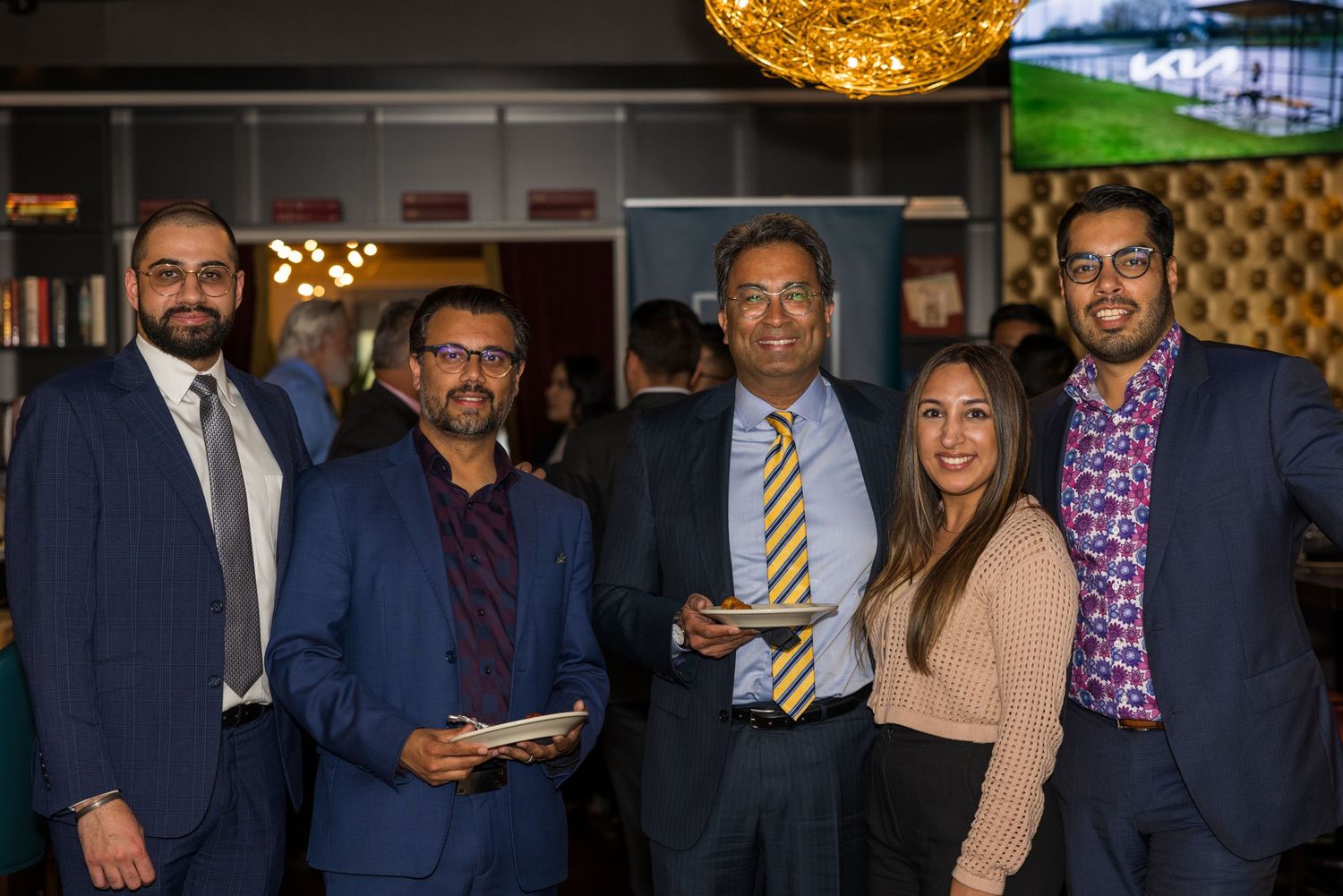 A group of professionals networking at an evening business event under warm lighting.