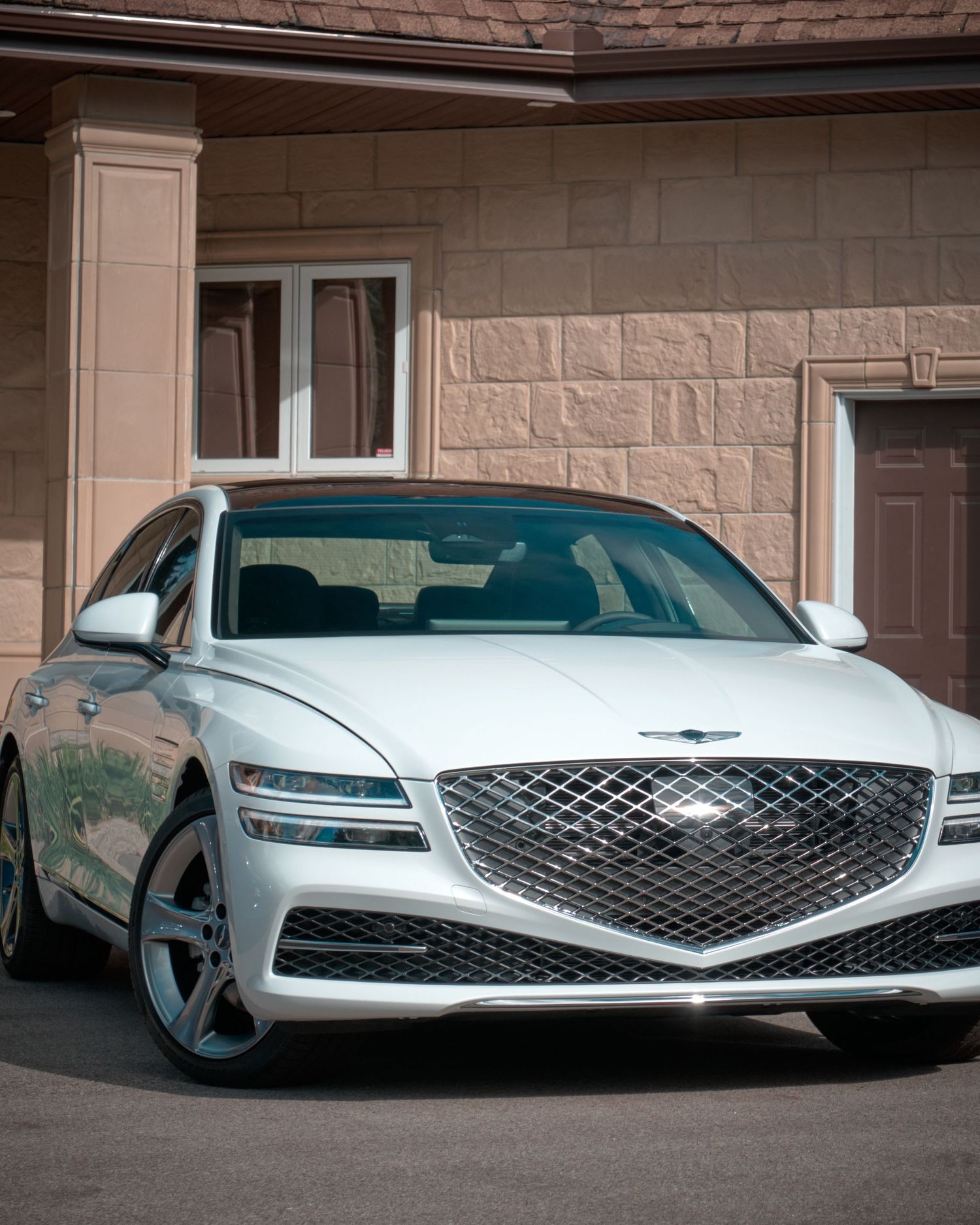 White Genesis luxury sedan showcasing its distinctive front grille and sleek design against stone building.