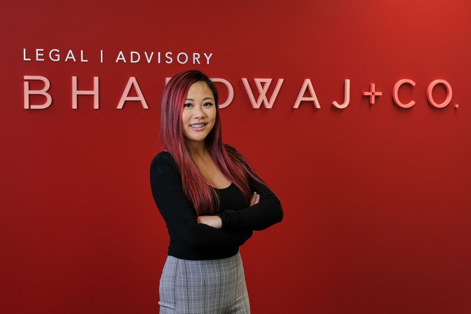Young professional poses confidently in front of red Bhardwaj Co wall signage.