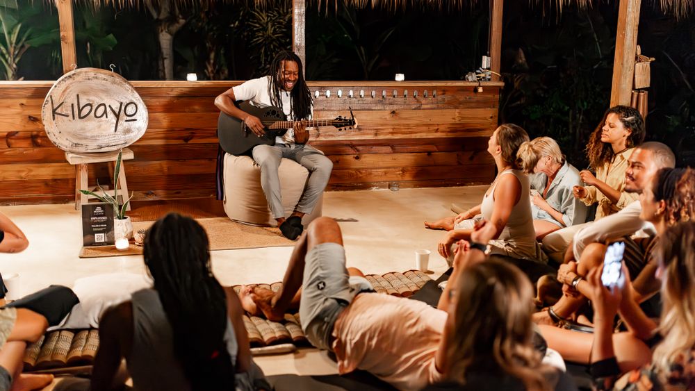 Musician performing for seated audience in tropical tiki bar setting.