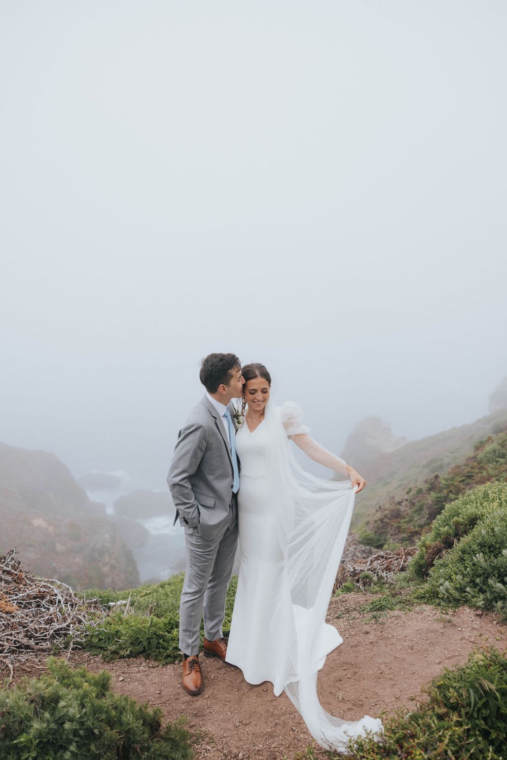 A bride and groom stand by a stunning overlook in Big Sur, CA while taking portraits with their wedding photographer.