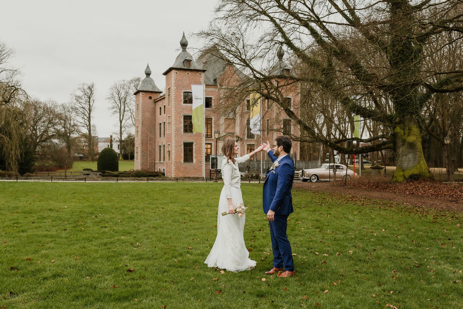 A wedding couple poses in front of a pink castle-like building on a manicured lawn.