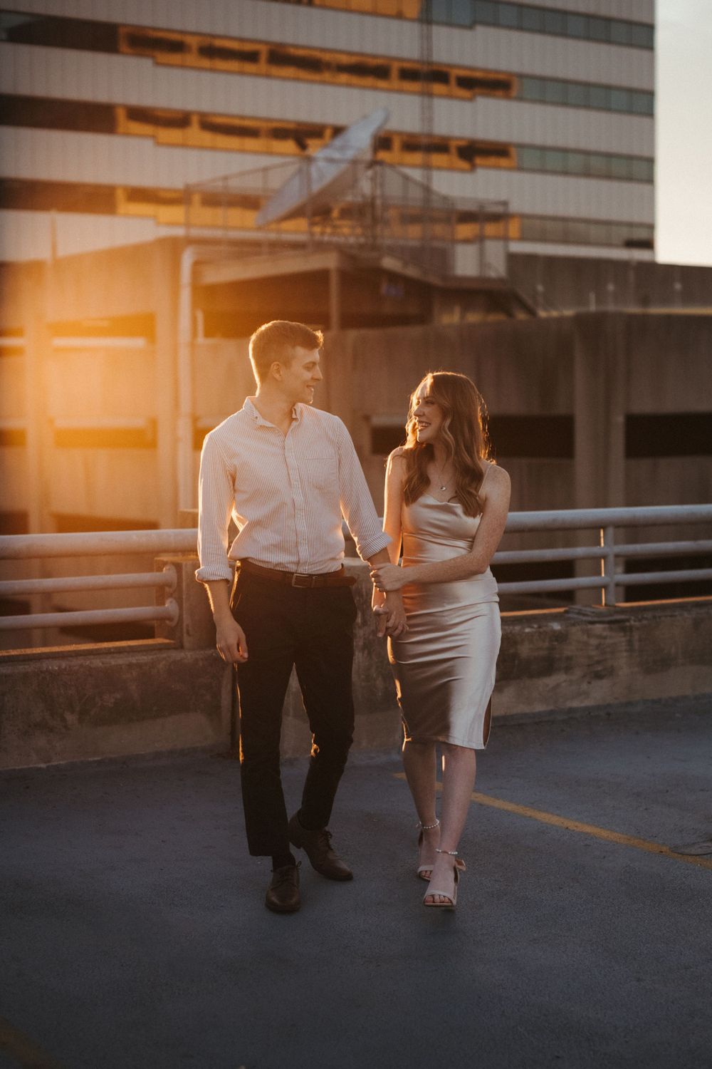 A couple walks together on a rooftop parking garage during golden hour sunset.