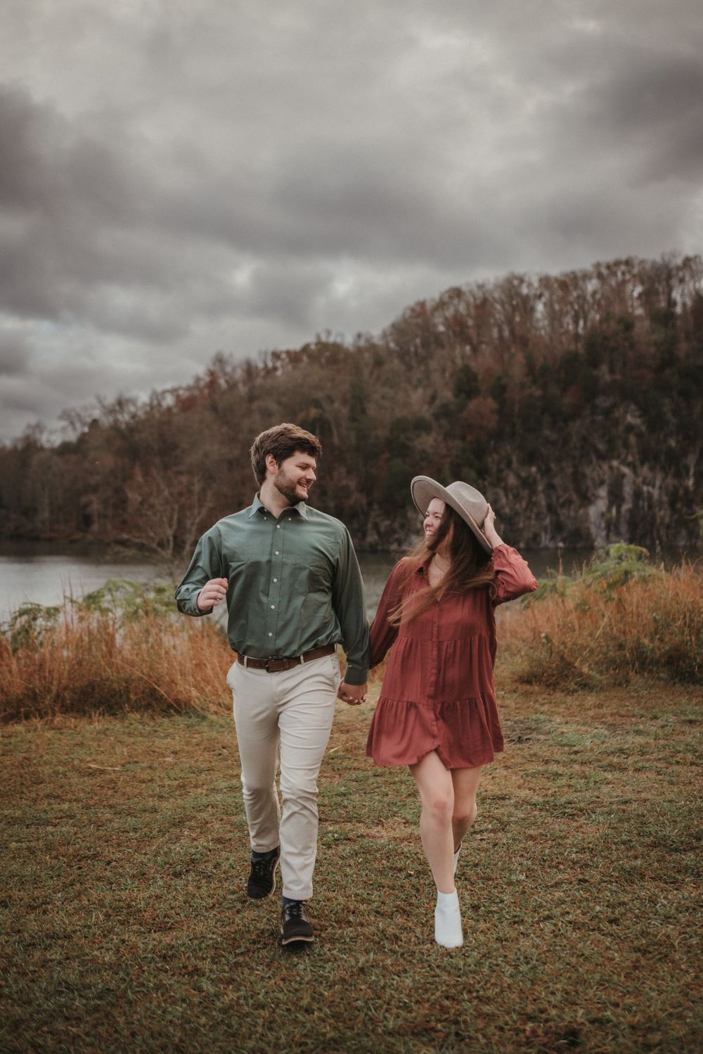 A couple walks hand in hand through an autumn field with moody overcast skies.
