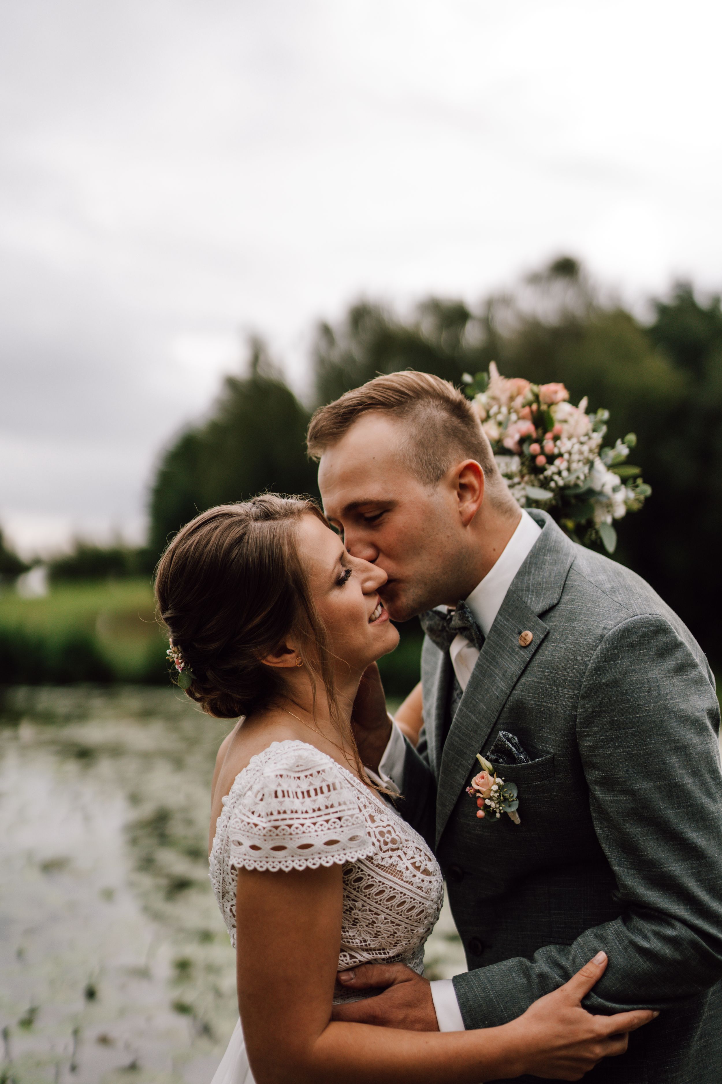 Intimate wedding portrait by lake with natural scenery in background.
