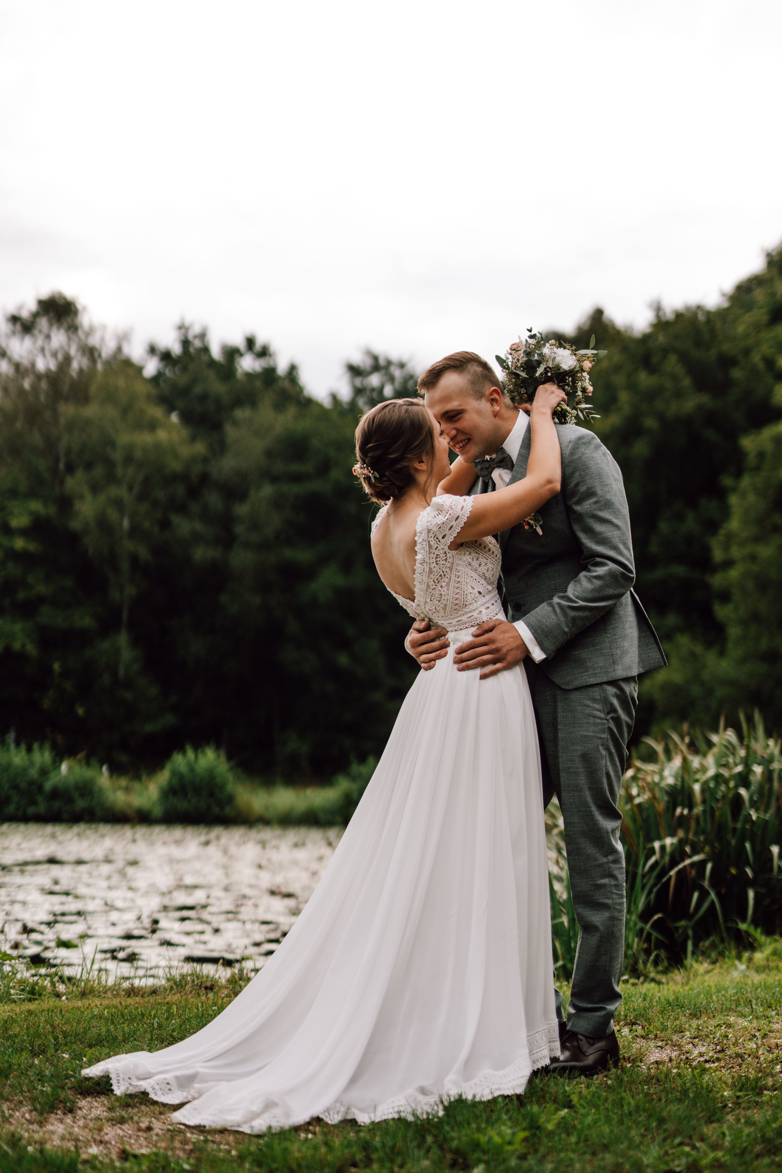 Romantic wedding moment captured by lake with natural landscape backdrop.