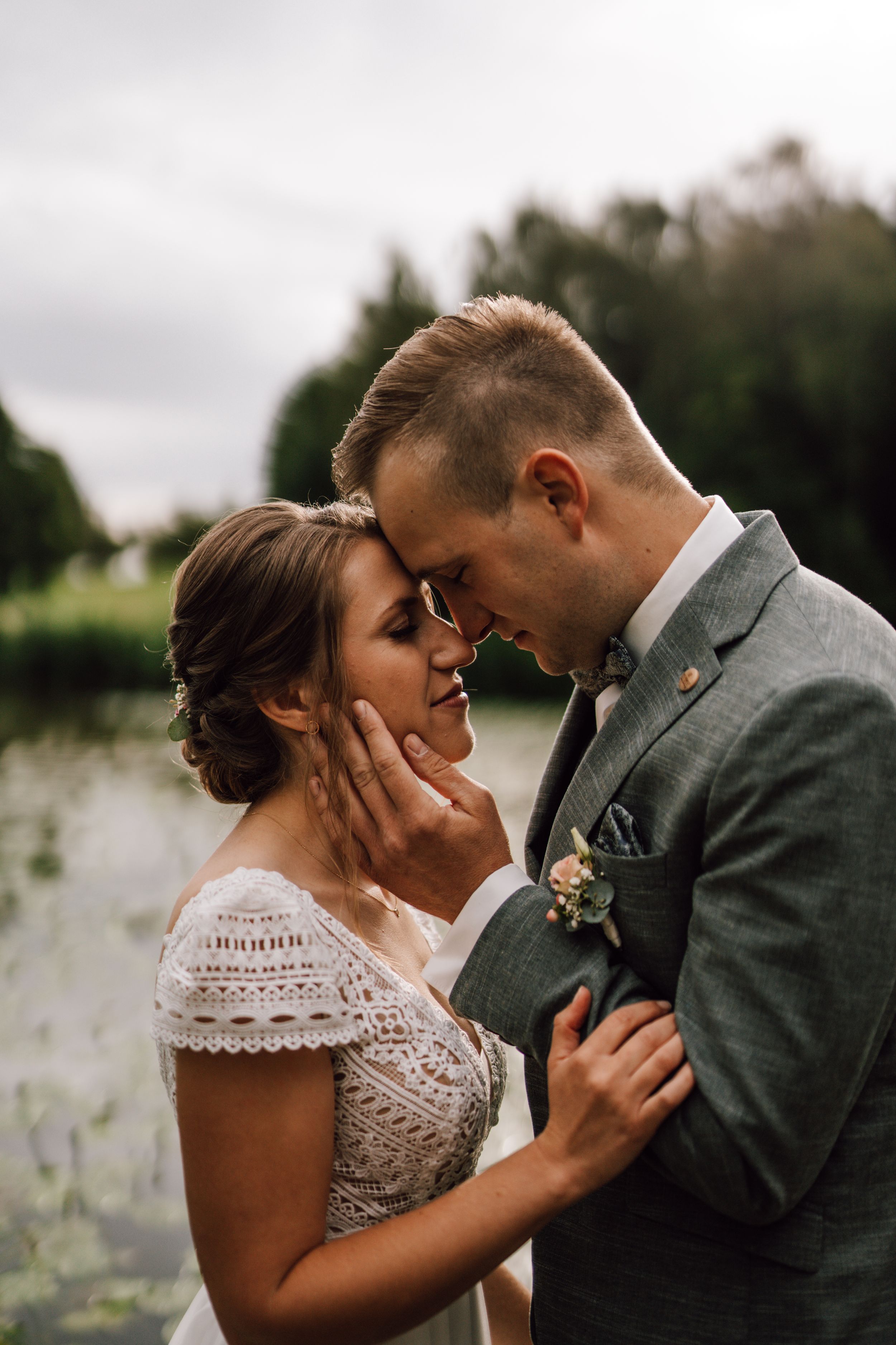 Tender moment between newlyweds against natural outdoor setting.