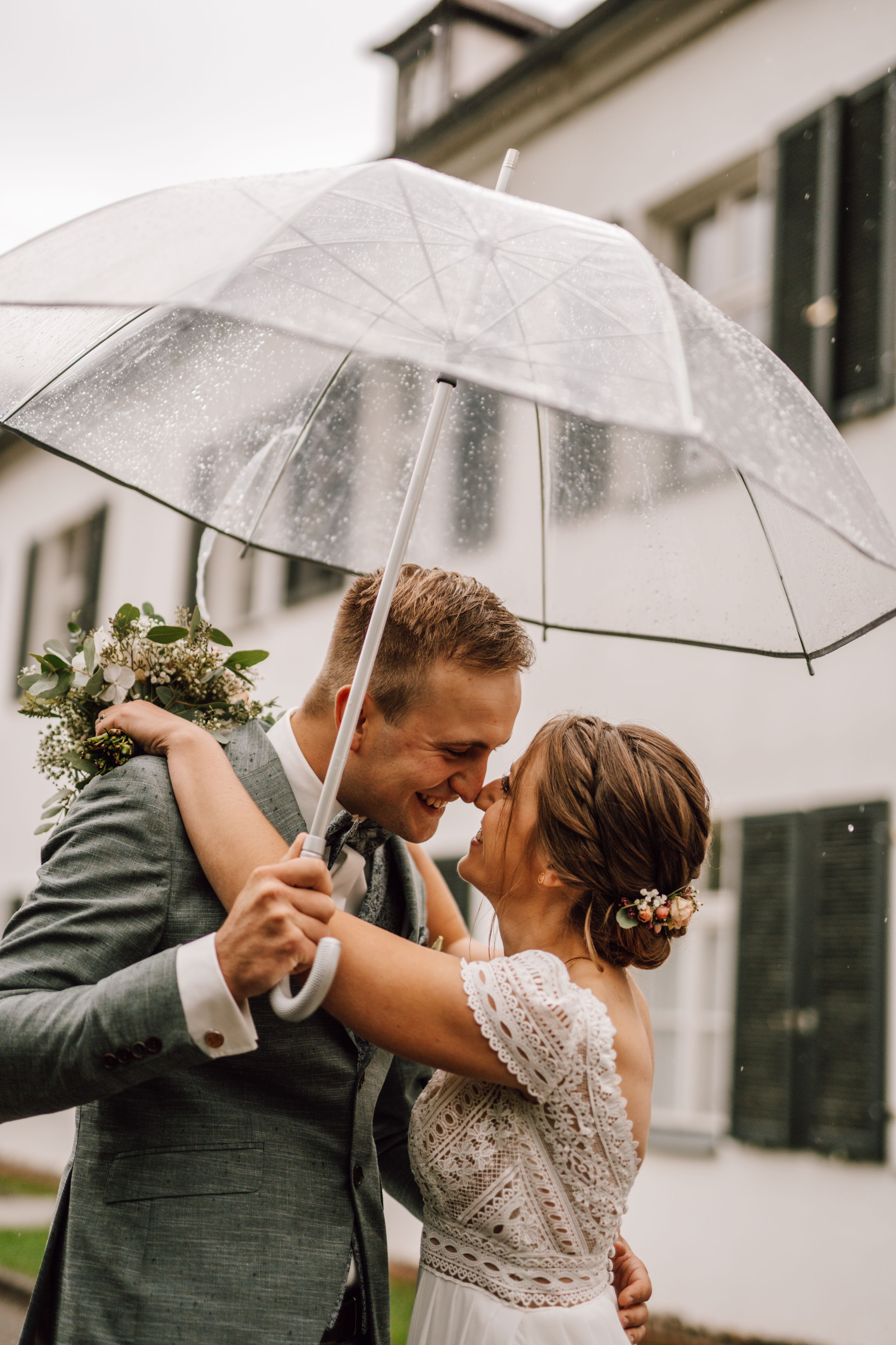 Romantic rainy day wedding moment shared under transparent umbrellas.