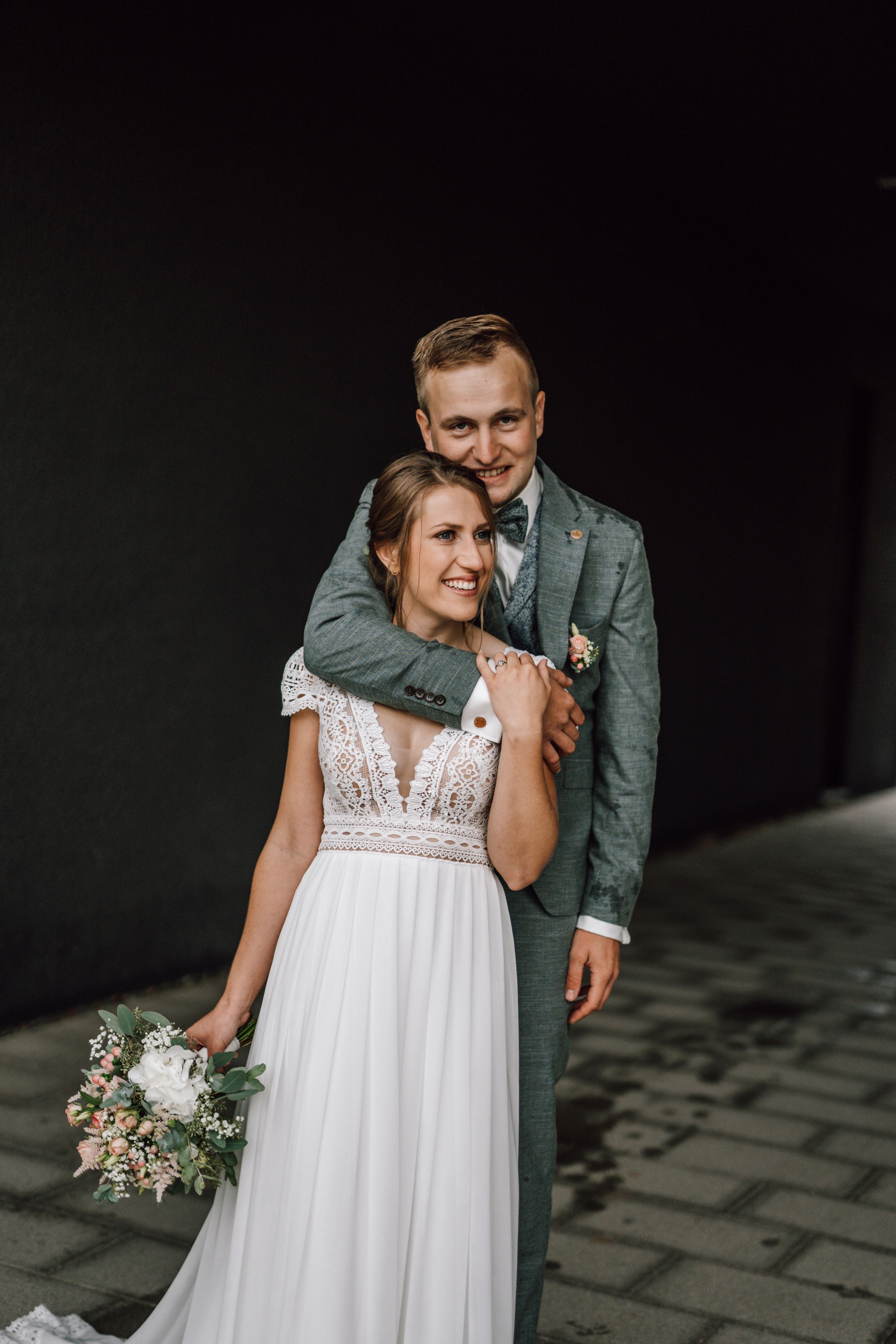 Intimate wedding portrait against dark background showing elegant lace dress details.
