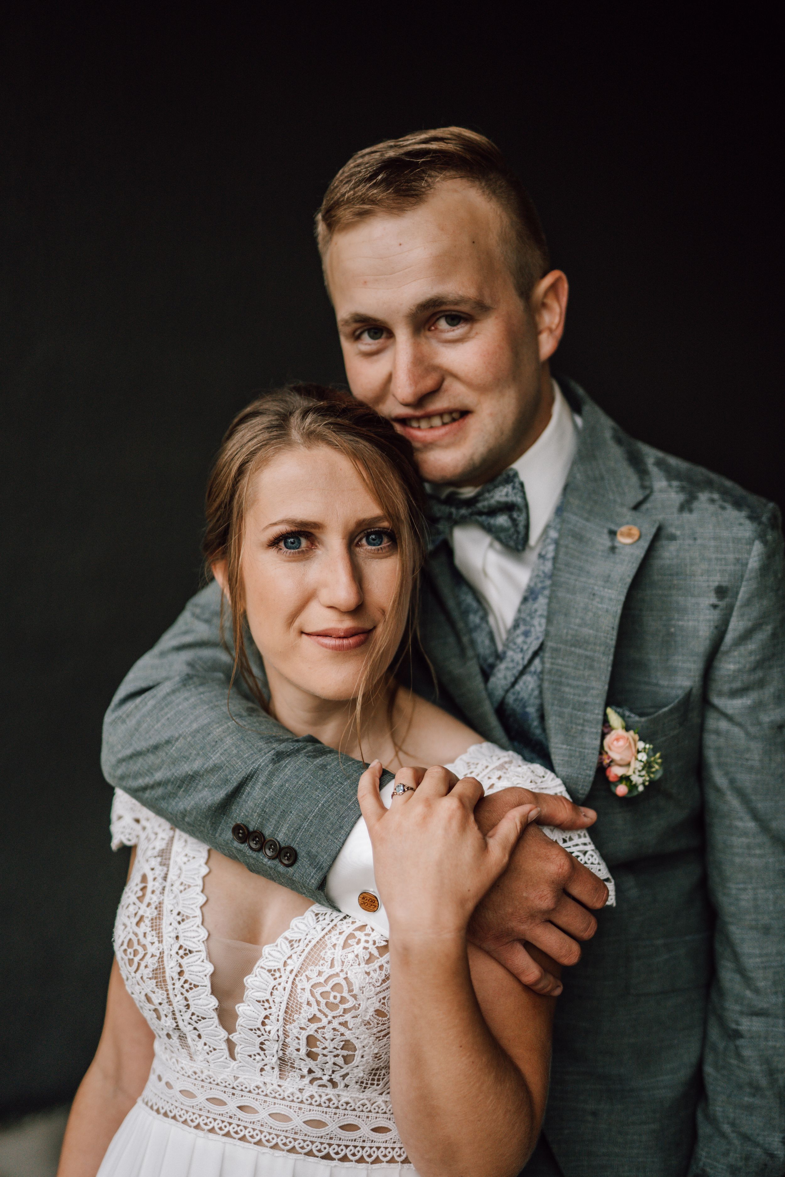 Wedding couple embracing in dramatic studio lighting showing detailed lace gown.