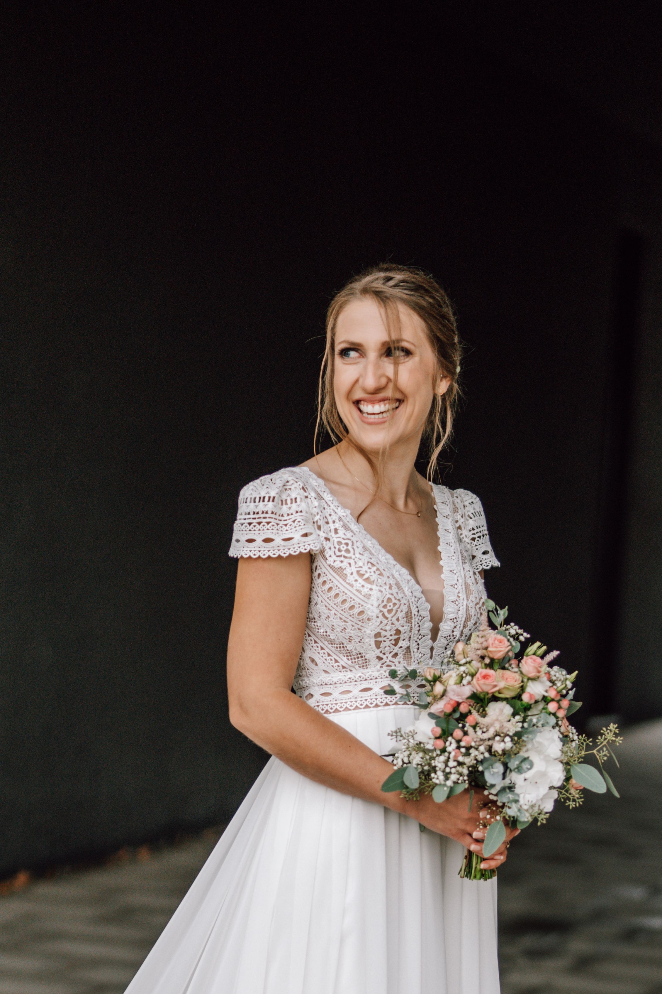 Bride holding delicate pastel bouquet in elegant lace wedding dress.