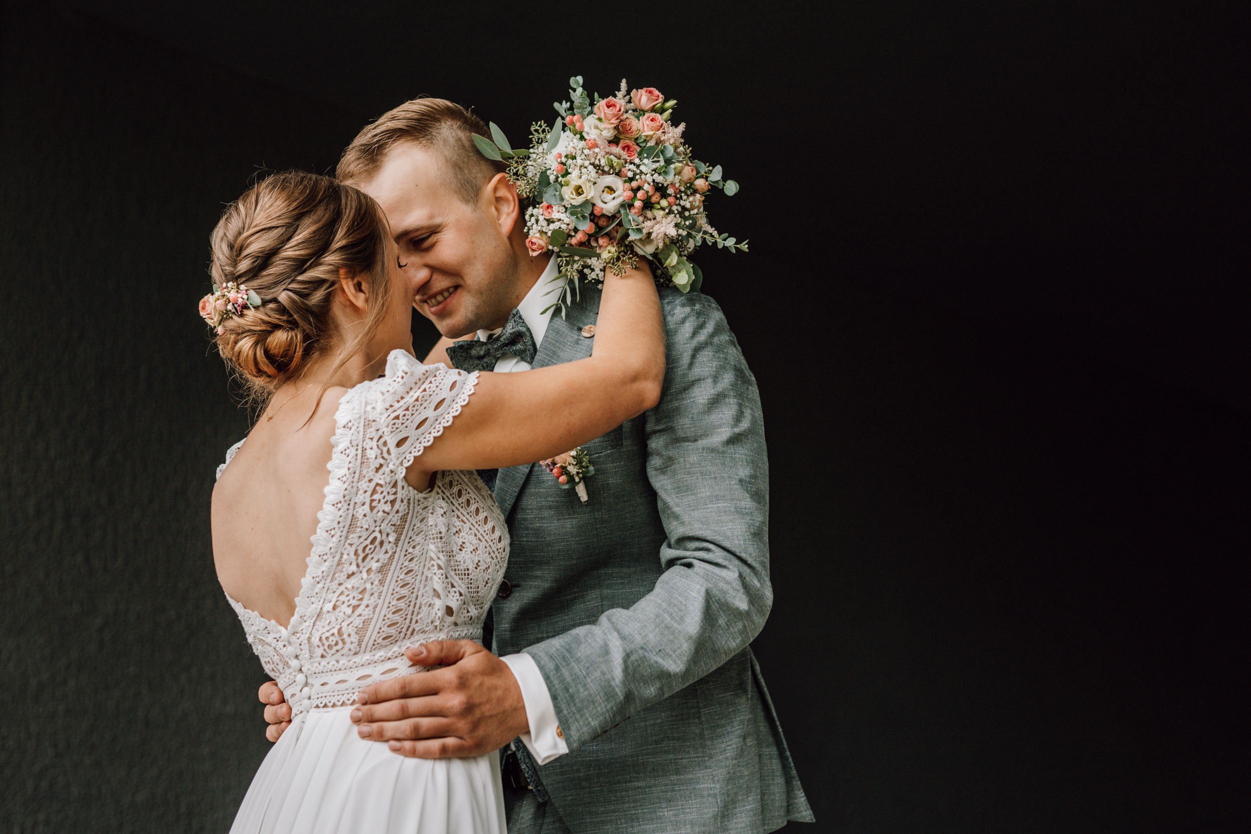 Romantic wedding moment with couple embracing against dark background with bridal bouquet.
