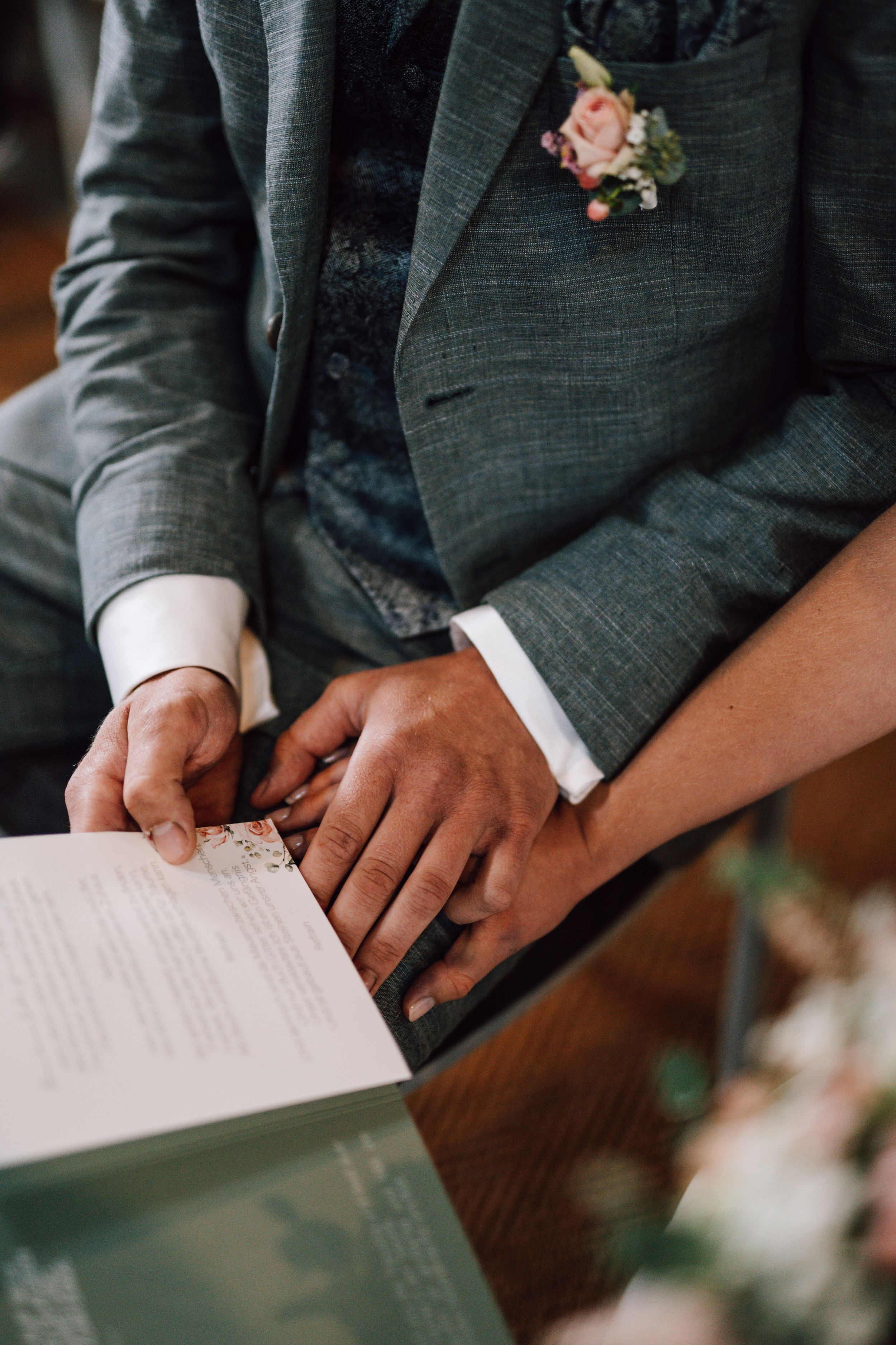 Close-up of groom in grey suit with pink boutonniere signing wedding documents.