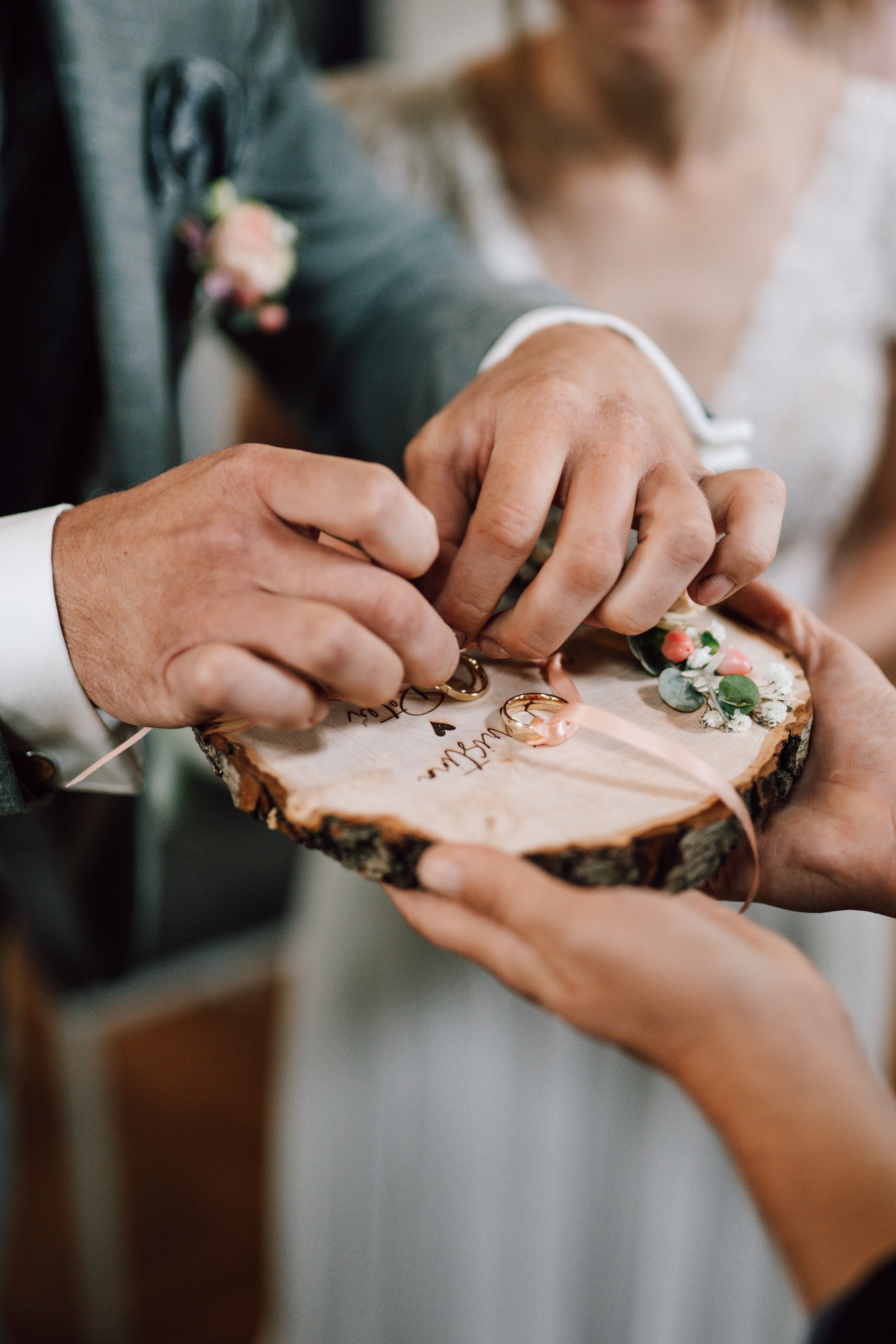 Hands holding wooden slice with engraved names during wedding ceremony.