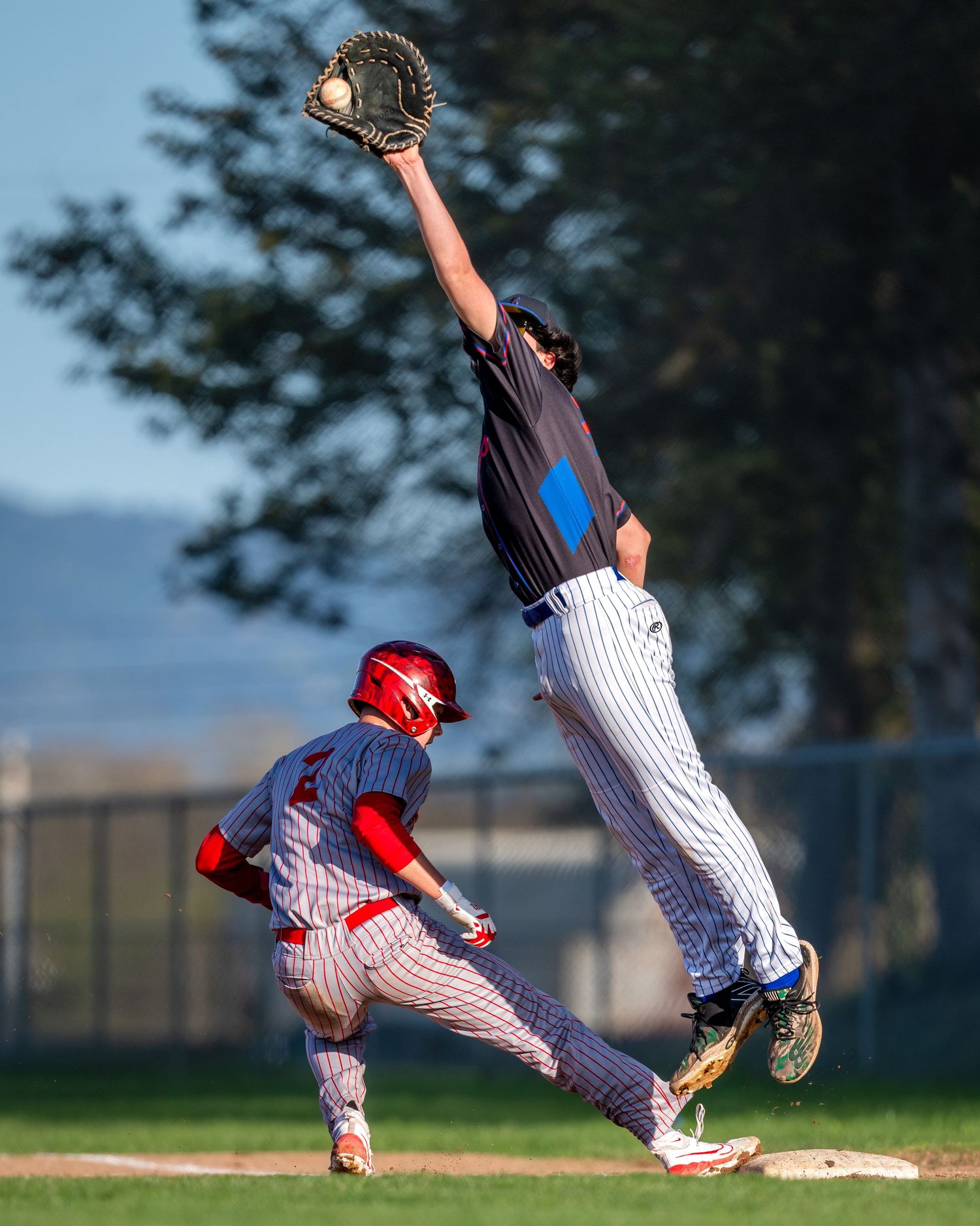 Baseball player leaping high to make defensive catch while runner in red helmet approaches base.