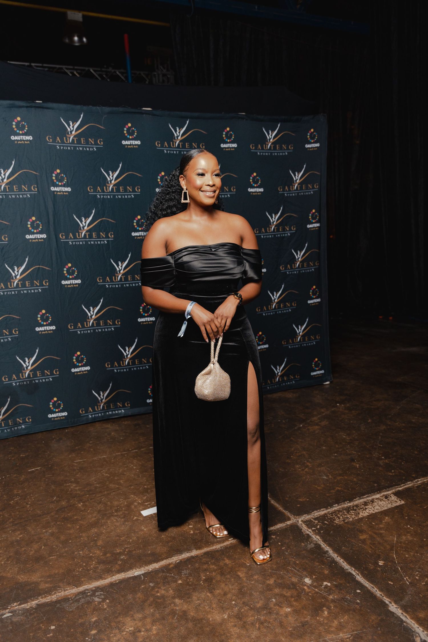 Elegant event photo featuring attendee in black formal dress with sequined purse against backdrop.