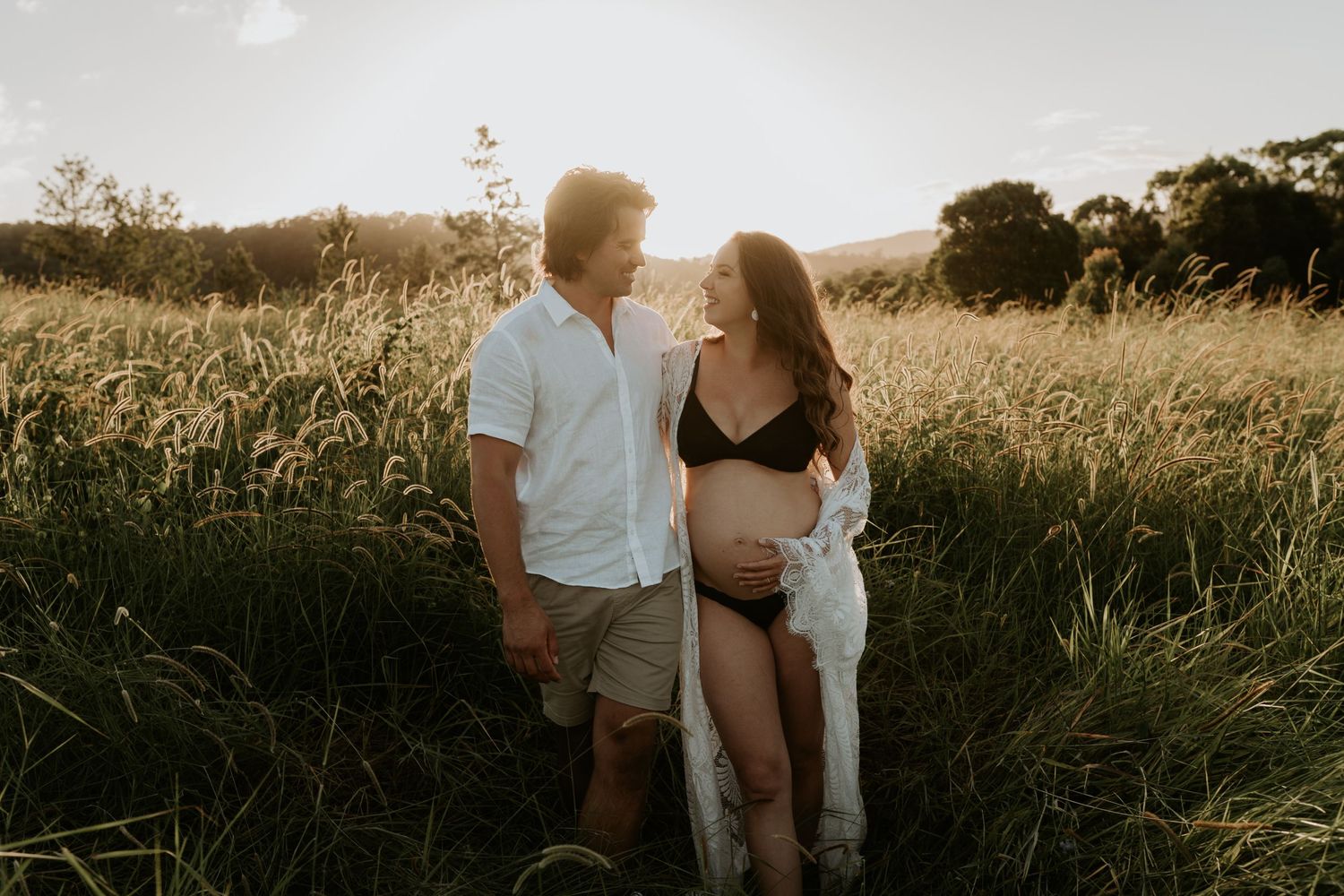 Romantic couple embracing in tall grass during sunset with dreamy warm lighting and natural scenery.