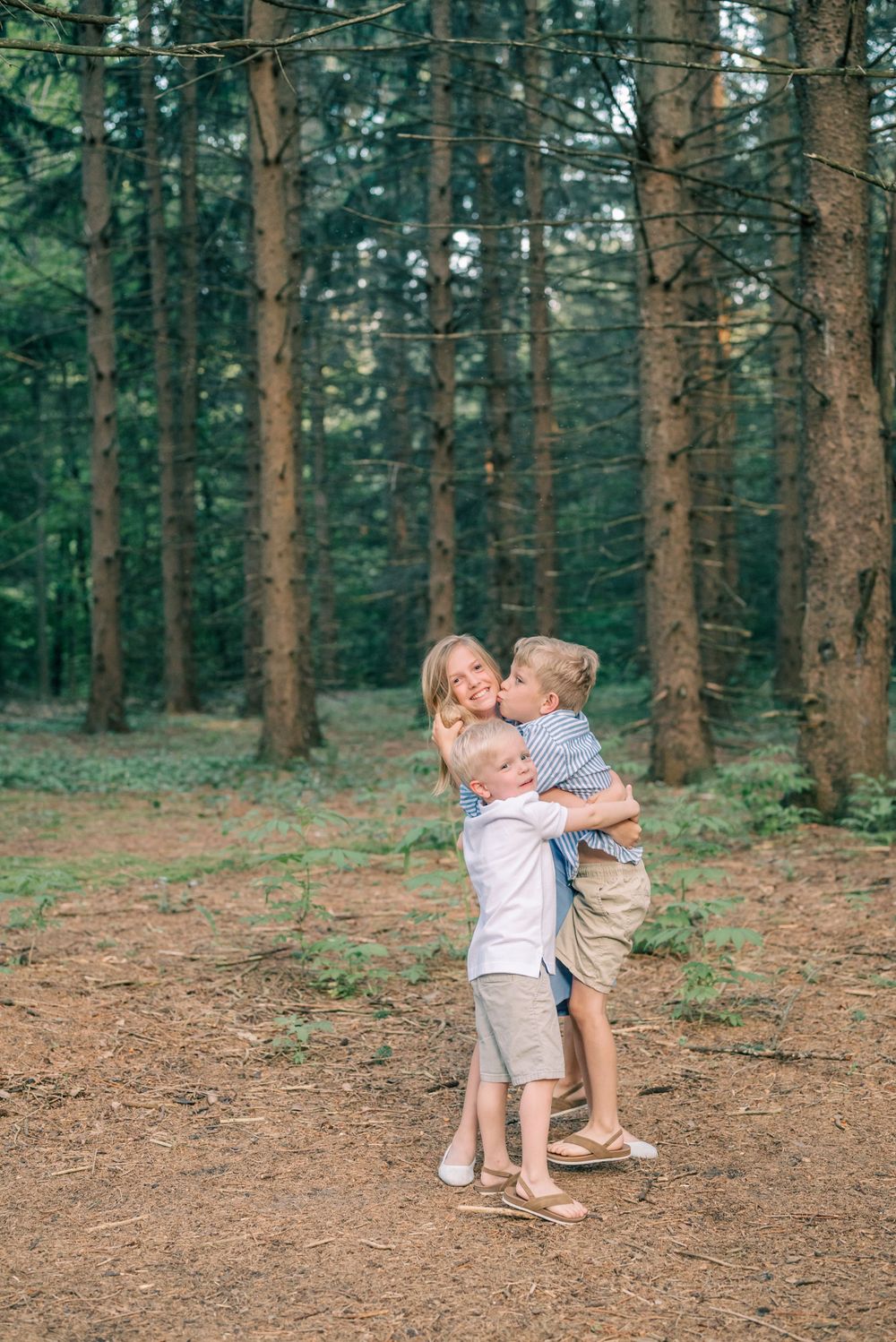 Two children hugging and playing in a pine forest.
