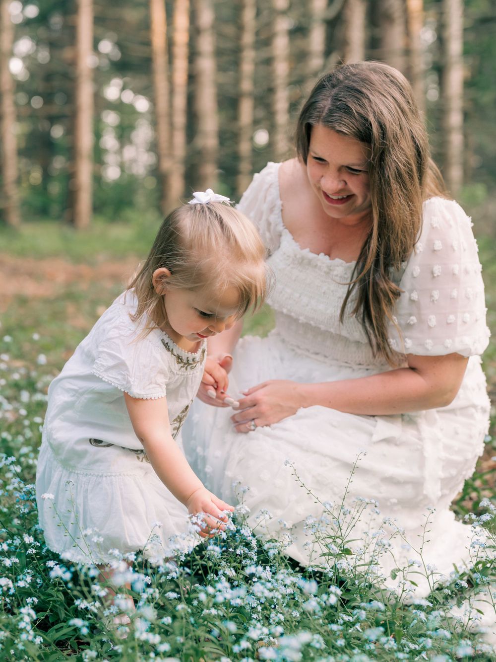 A touching moment in a forest as white-clad figures gather wildflowers among delicate spring blooms.
