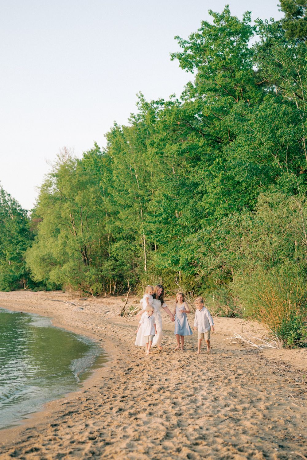 People in light summer dresses walking along a peaceful beach shoreline at sunset.