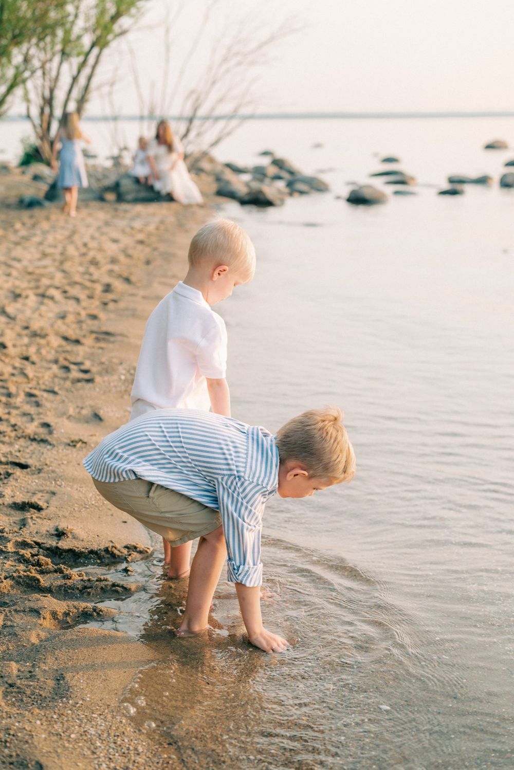Children in casual summer clothes playing and exploring at the water's edge on a sandy beach.