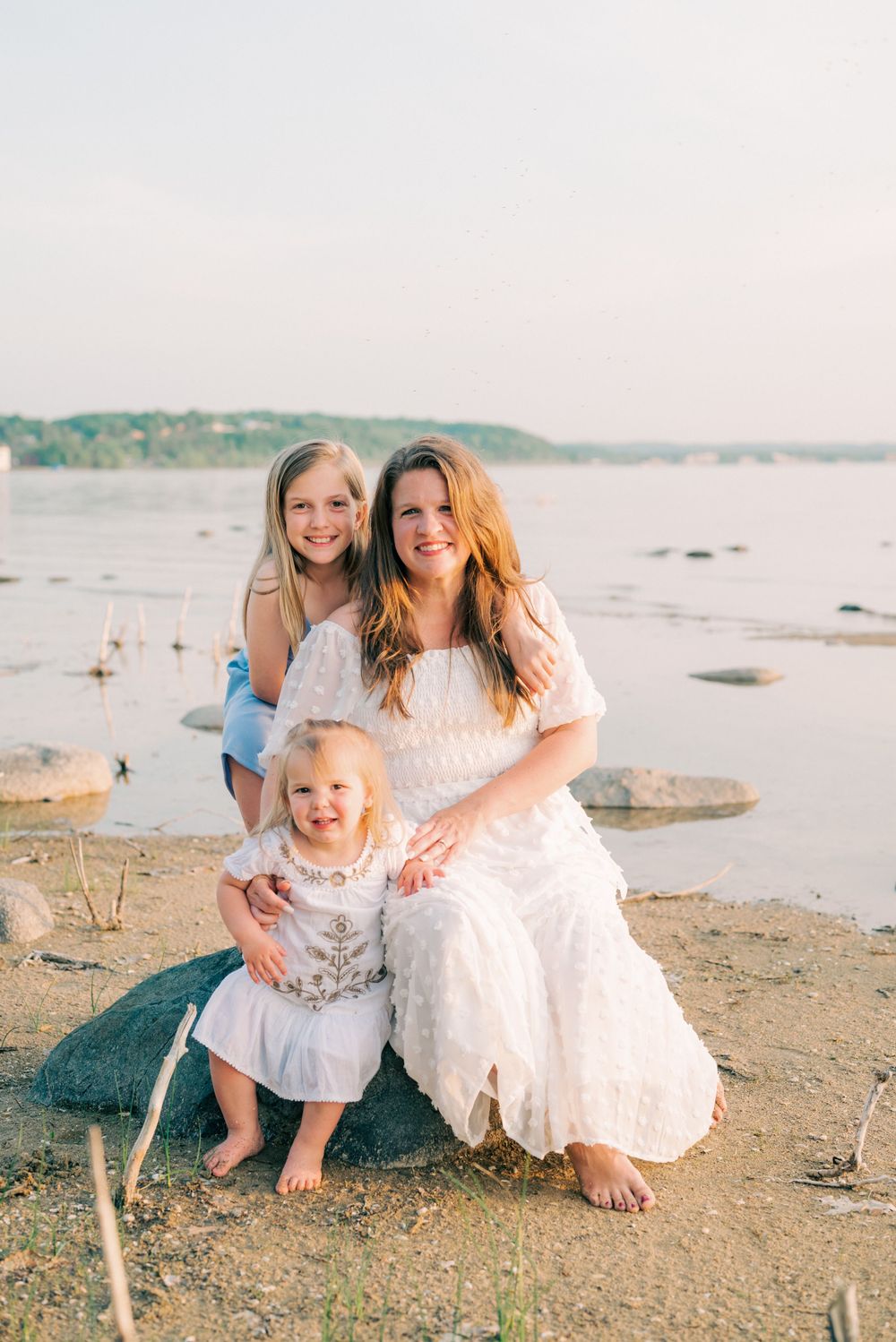 A heartwarming beach portrait with figures in white dresses against a serene waterfront backdrop.